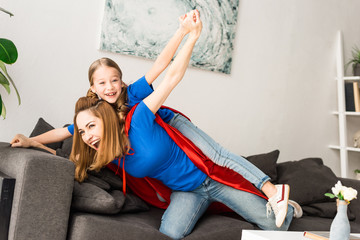 Smiling mother and daughter in red cloaks playing at home