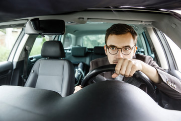 Young driver is driving his car. He is holding steering wheel with both hands. He is looking at the road.