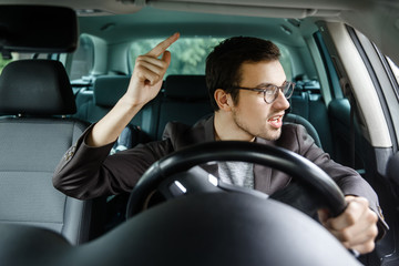 Wall Mural - Angry young driver quarrels with other drivers. His left hand is on the steering wheel.