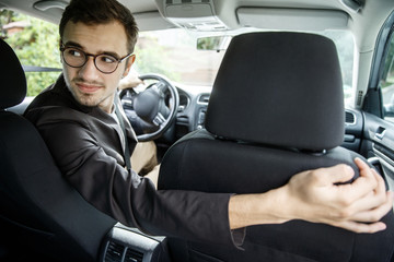 Wall Mural - Young taxi driver looks back over the seats. His right hand is on the seat. He is sitting at his car.