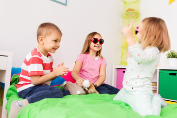 Poster - summer, valentines day and childhood concept - happy little kids in heart shaped sunglasses playing at home