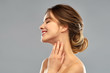 beauty and people concept - smiling young woman touching her neck over grey background