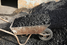 Pile Of Coal On An Old Rusty Wheelbarrow In Front Of An Old Wall On The Street
