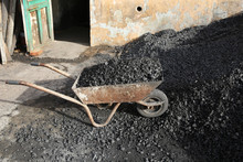 Pile Of Coal On An Old Rusty Wheelbarrow In Front Of An Old Wall On The Street