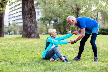 Wall Mural - Senior woman helping her husband to stand up after fall while they were jogging.