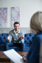 Man sits on the couch smiling and talking to a psychologist consultant.