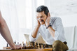© LIGHTFIELD STUDIOS - selective focus of senior man with mustache covering ears while playing chess with friend at home