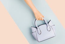Female Hands Holds Handbag On Blue Background . Flat Lay, Top View. Spring Fashion Concept In Pastel Colored