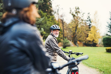 Active senior couple with electrobikes standing outdoors on a road in nature.