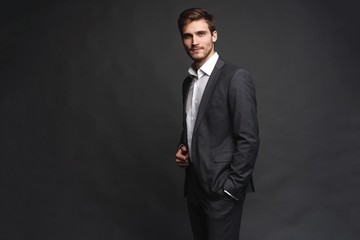 Wall Mural - Portrait of a handsome young businessman dressed in suit isolated over gray background.