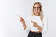 Energized Successful Good-looking Young Female Entrepreneur In Glasses And Sweater Smiling Pointing Left Amused And Entertained Feeling Excited At Awesome Course Gathering Over White Wall