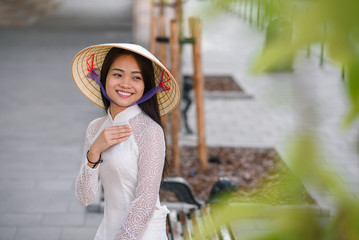 Close up portrait of pretty asian girl dressed in Ao Dai dress wearing vietnamese conical hat.