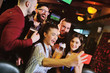 © Evgeniy Kalinovskiy - group or company of young people - friends drink beer, eat pizza, talk and laugh and shoot selfie on the smartphone's camera on the background of the bar