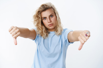 Wall Mural - Very bad, not like it. Portrait of dissatisfied and displeased good-looking young blond female with tanned skin and blue eyes tilting head frowning in disagree showing thumbs down from dislike