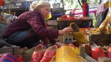 On A Beautiful Sunny Day A Beautiful Blonde Tourist Chooses A Typical Dutch Clog In A Craft Fair. Amsterdam Netherlands. Flat Plane