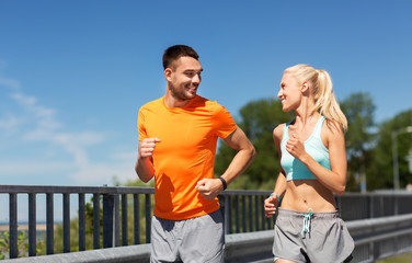 Wall Mural - sport, technology and lifestyle concept - happy couple with fitness trackers running along bridge in summer