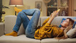 © VAKSMANV - Happy girl lying on sofa using a smart phone at home.