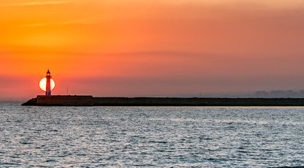 Wall Mural - Sun setting behind lighthouse over the ocean.