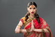 indian woman in traditional clothing and accessories with namaste mudra, isolated on grey