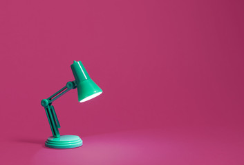 retro green desk lamp turned on and bent over shining on a bright pink background. landscape orienta