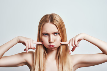 Studio shot of stubborn young blonde woman blowing cheeks and feeling mad. Human emotions.