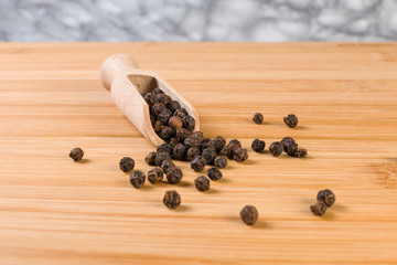 Black pepper peppercorns in wooden scoop on bamboo desk. Closeup.