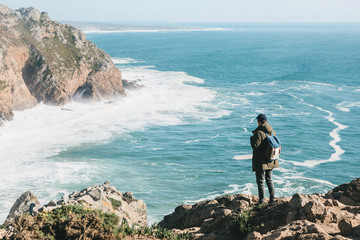 Wall Mural - A man tourist with a backpack stands in solitude at Cape Roca in Portugal and enjoys a beautiful view of the Atlantic Ocean.