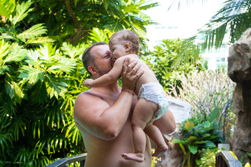 Dad holds his baby. Father and daughter together outdoors, dad kisses and hugs his daughter, moved by the children. Green background Active family concept. Room for copying text.