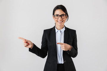 Portrait of european businesswoman 30s in formal wear and eyeglasses pointing fingers aside, isolated over white background