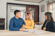 © tirachard - Happy young Asian couple and realtor agent. Cheerful young man signing some documents while sitting at desk together with his wife. Buying new house real estate. Signing good condition contract.