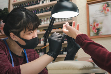 Wall Mural - The manicurist in black latex gloves covers the client's nails with a transparent gel polish in the beauty salon.