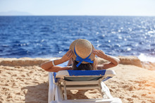 Beautiful Woman Sunbathing On A Beach At Tropical Travel Resort, Enjoying Summer Holidays. Young Woman Lying On Sun Lounger Near The Sea. Happy Serene Woman