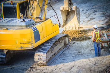 Civil engineer foreman is supervising backhoe to digging for earthwork in highway construction site.