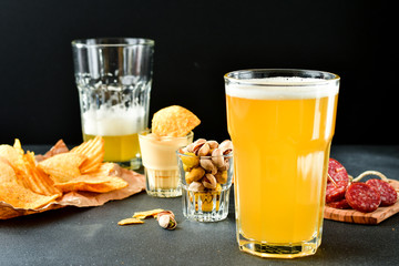 two glasses of beer and snacks chips, nachos with sauce, pistachios and salami, aperitif, relax in the bar with friends, beer party.  selective focus and copy space