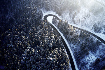 Wall Mural - Aerial drone view of a curved winding road through the forest high up in the mountains in the winter with snow covered trees and curved streets in winter