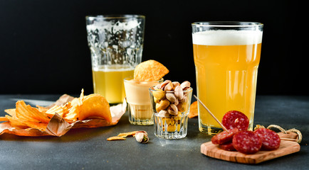 two glasses of beer and snacks chips, nachos with sauce, pistachios and salami, aperitif, relax in the bar with friends, beer party.  selective focus and copy space