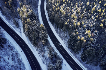 Wall Mural - Aerial drone view of a curved winding road through the forest high up in the mountains in the winter with snow covered trees and curved streets in winter