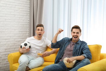 Canvas Print - Men with snacks and ball watching soccer match on TV in living room