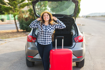 Wall Mural - Happiness, travelling and people concept - young woman standing near back of car smiling and getting ready to go. Summer road trip