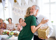 Young woman giving a gift to her grandfather on indoor party, hugging.