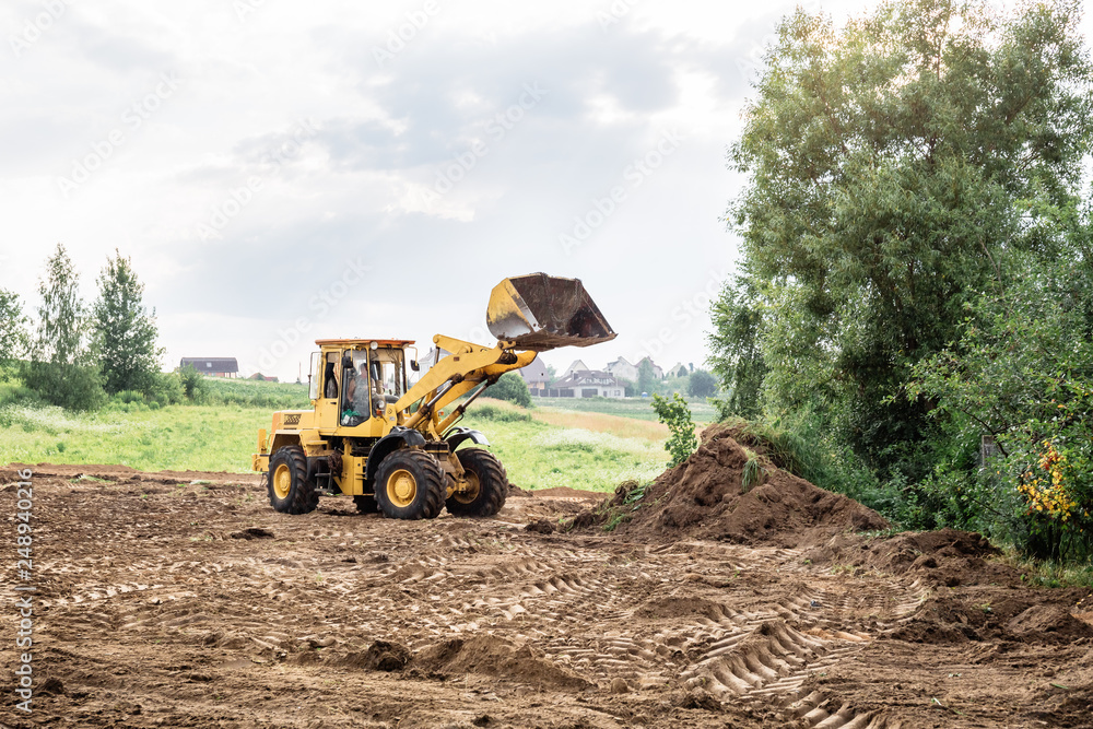 large yellow wheel loader aligns a piece of land for a new building. May be cut to banner or wallpaper with copy space. - obrazy, fototapety, plakaty 