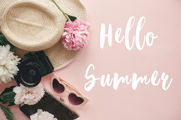 Wall Mural - Hello Summer text sign on stylish photo camera, retro sunglasses, hat, peonies on pastel pink paper. Summer vacation and travel concept, girly image