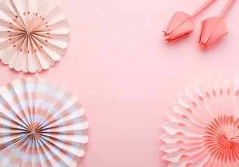 Chinese paper fans in pastel colors on pink table, top view, copy space for text, selective focus. Paper flowers in living coral.