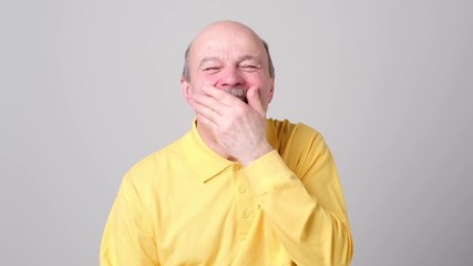 Poster - Mature man laughing and covering his mouth with hand over white background.