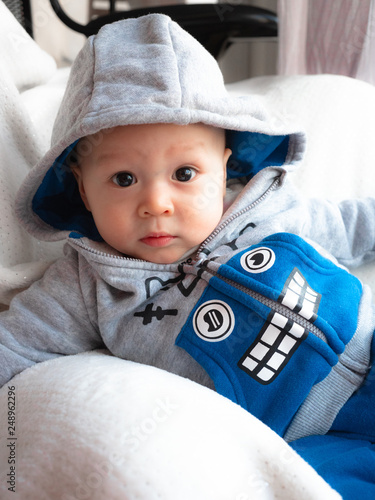 Portrait Of Cute Adorable Caucasian Smiling Laughing Baby Boy With Black Eyes In Grey Blue Hoodie