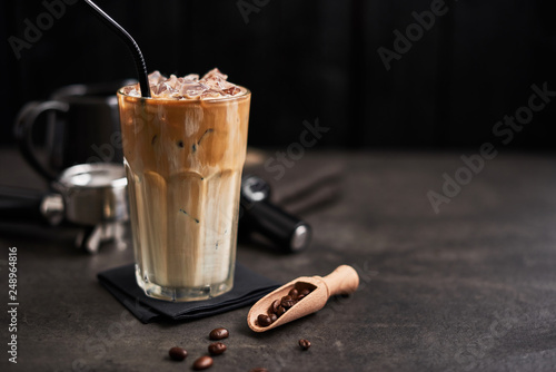 Fotomural Ice coffee with cream in a tall glass and coffee beans, portafilter, tamper and milk jug on dark concrete table over black wooden background