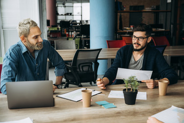 Wall Mural - The working process. Two successful guys discussing business during work day and work with laptop and documents. Coworking.