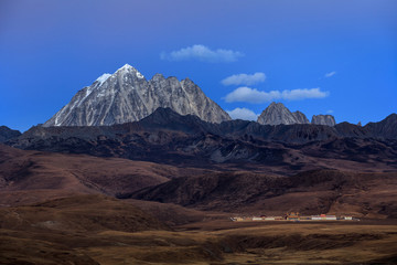 Wall Mural - Tagong Prairie Grassland, Lhagang Grassland, Tibetan area of Sichuan Province China. Buddhist Monastery in foreground, Yala Snow Mountain towering in the distance. Twilight, martian alien landscape