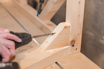 Wall Mural - A man is screwing a screw into a wooden table. Carpentry workshop. Work with a screwdriver.