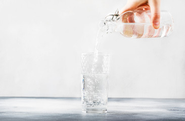 Clear water is poured from glass bottle into glass, gray background, selective focus